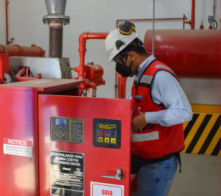 Técnico especialista realizando mantenimiento preventivo a un controlador de bomba contra incendios diésel en cuarto de máquinas.