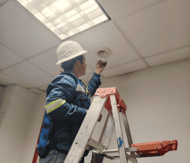 Técnico revisando detector de humo durante mantenimiento de sistema de detección