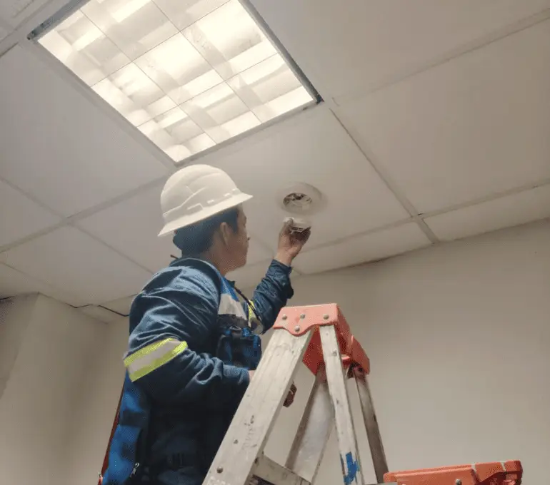 Técnico de FireTech Solutions inspeccionando detector de humo en mantenimiento preventivo